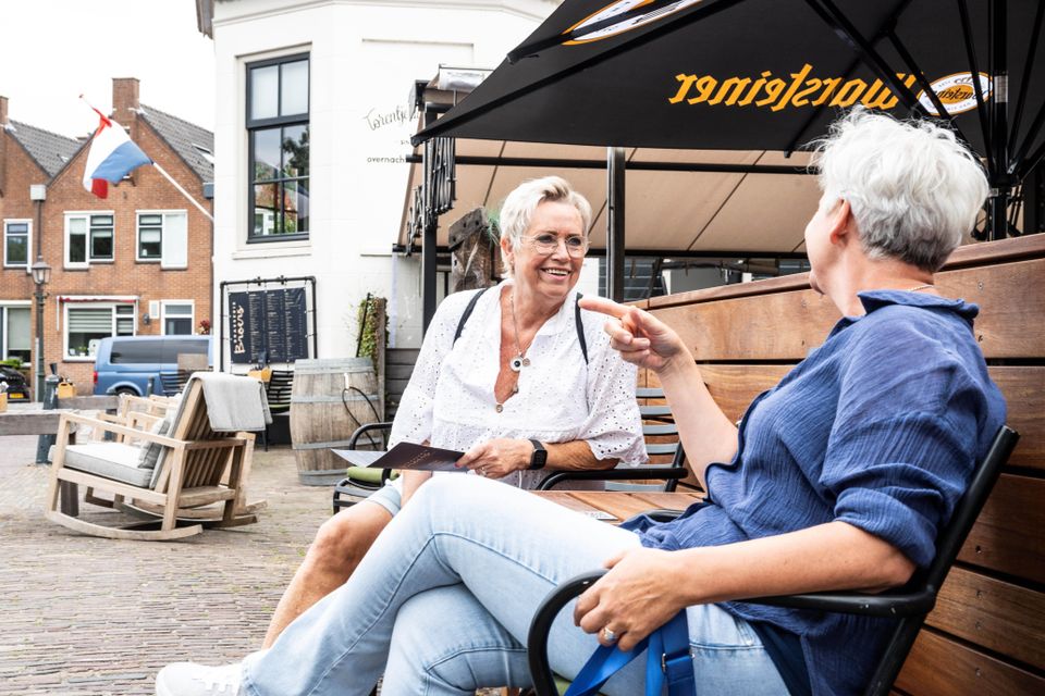 Accommodatie Torentje aan de IJssel in Montfoort, Groene Hart, buitenzitje aan de kade met twee bezoekers in gesprek onder parasol, historisch straatbeeld aan de Hollandse IJssel.