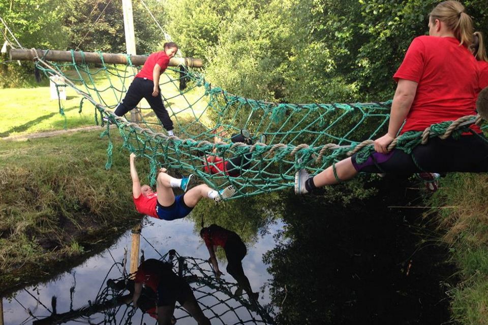 Mensen klimmen via een net over het water tijdens een teambuildingsuitje.