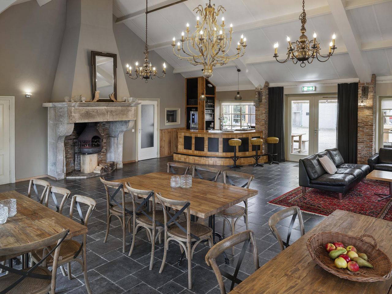 Grote zaal met antieke schouw, kroonluchters, een bar en diverse sitjes.