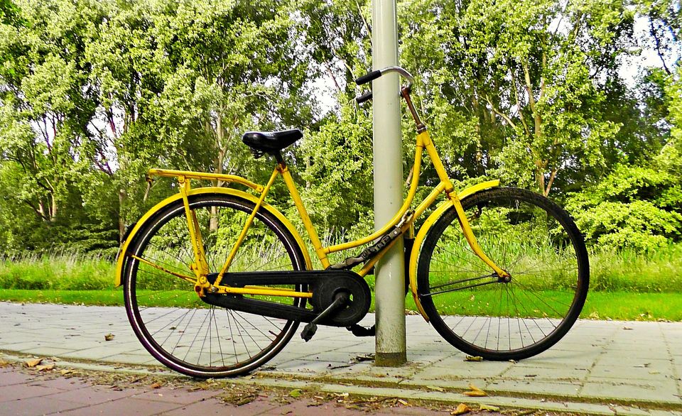 Een gele fiets staat tegen een lantaarnpaal aan. Hij is vastgemaakt met een slot.