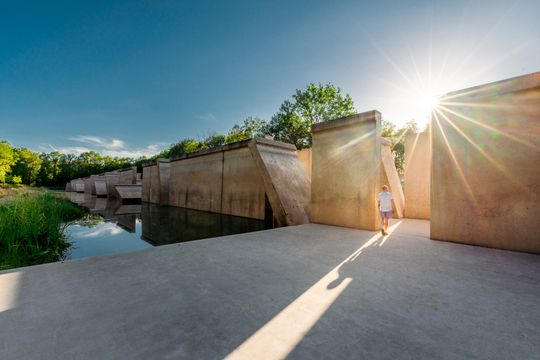 Een man kijkt naar grote betonnen panelen die soms dwars staan. De oorspronkelijke functie van deze panelen was een Deltagoot. Dit staat in het Waterloopbos in de Noordoostpolder.