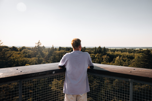 Een man kijkt hoog boven de bomen uit over het weidse Drentse landschap vanaf de de uitkijktoren Poolshoogte.