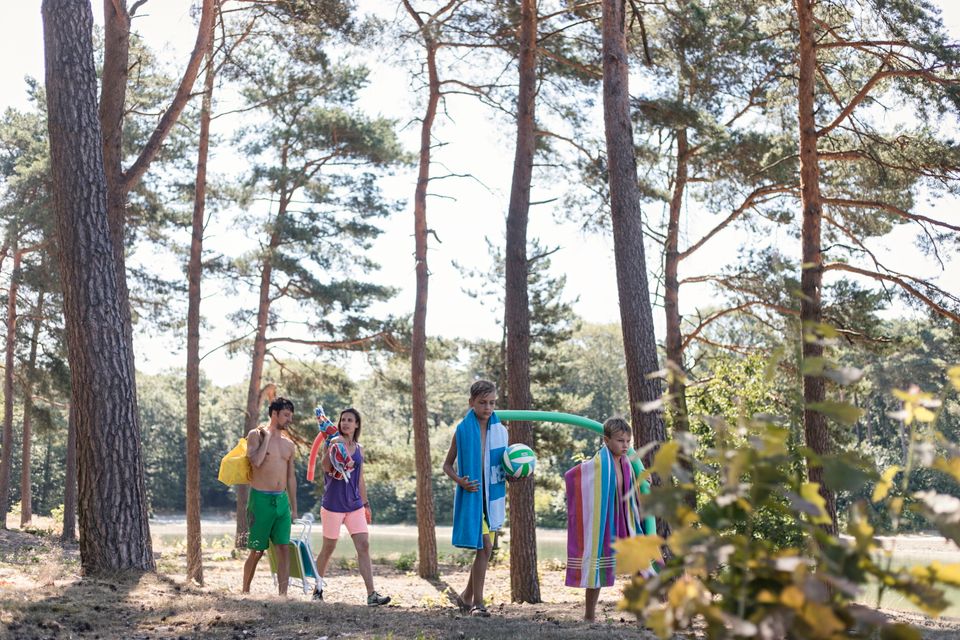 Een gezin komt met handdoeken, ballen en ander speelmateriaal aanlopen bij zwemplas Kibbelkoele.