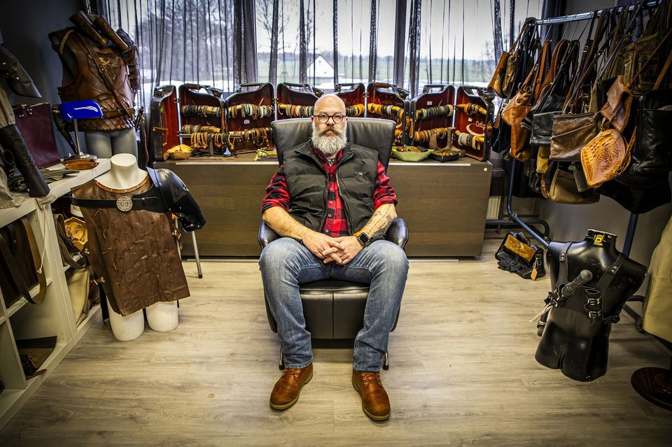 Eigenaar van Handmade by Ortlep zit in zijn werkruimte tussen handgemaakte leren tassen, armbeschermers en andere producten.