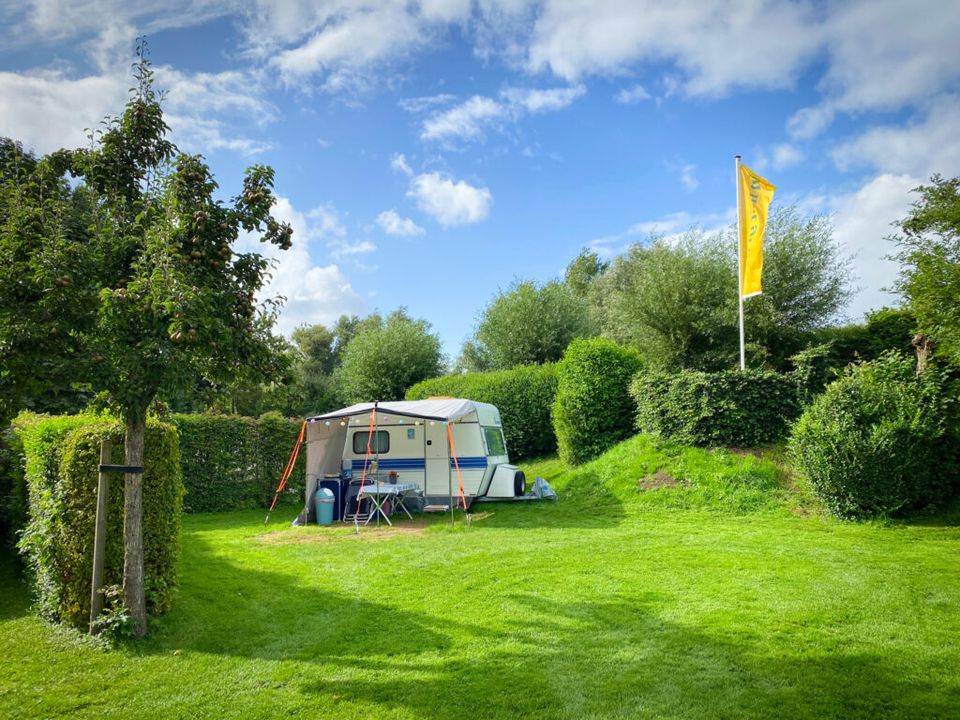 een witte caravan in een groen grasveld omgeven door veel heggen.