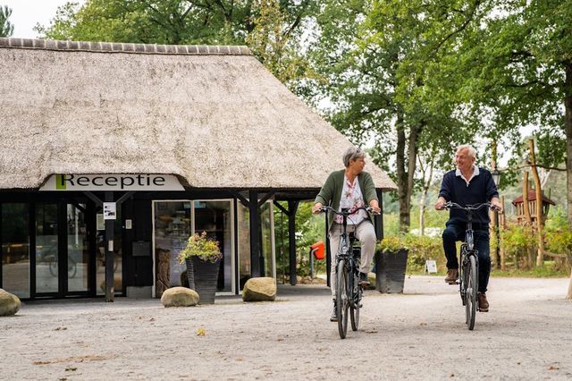 Ein älteres Paar fährt mit dem Fahrrad an der Rezeption eines Campingplatzes in Drenthe vorbei.