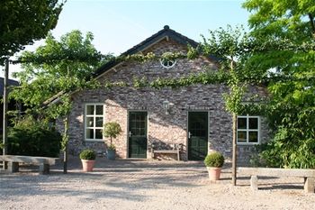 Vooraanzicht van één van de gebouwen in oude stijl met grindpad en leibomen.