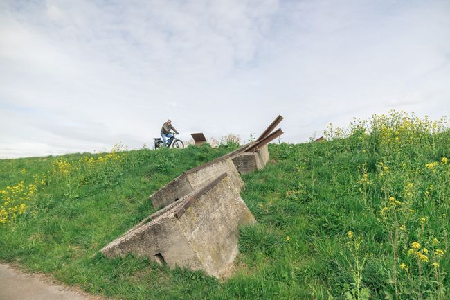 Fietser passeert een zichtbaar verdedigingswerk van de Grebbelinie in het groene buitengebied van Bunschoten-Spakenburg. De foto combineert recreatief fietsen met militair erfgoed en het open landschap.