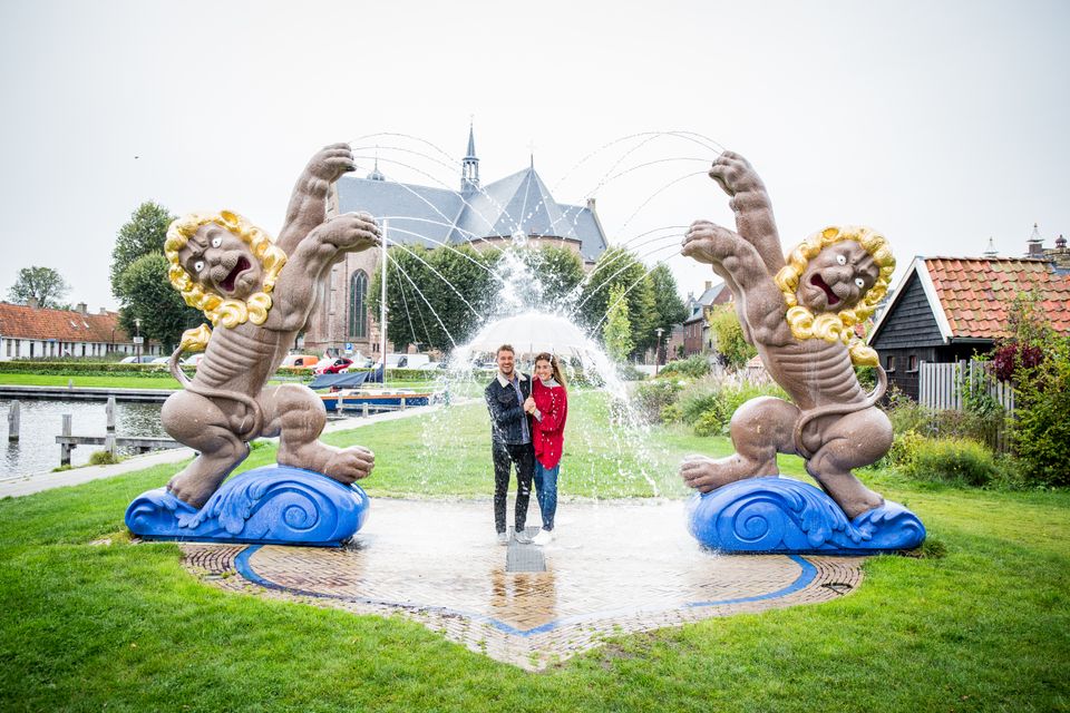 Een man en en vrouw staan met een paraplu onder de fontein in Workum.