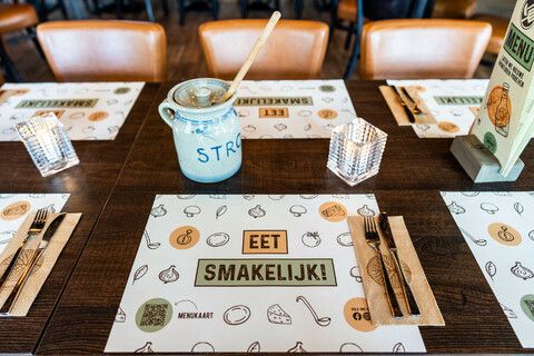 Een gedekte tafel met stroop en een placemat waar eet smakelijk op staat.