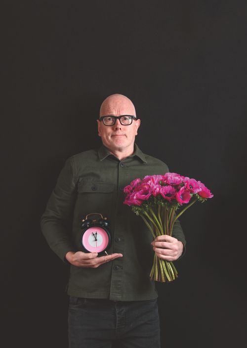 Een man met een blos bloemen en een wekker in zijn handen