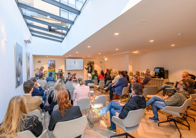 Overzichtsfoto van de zaal tijdens de Partnerbijeenkomst. Publiek luistert naar een presentatie.
