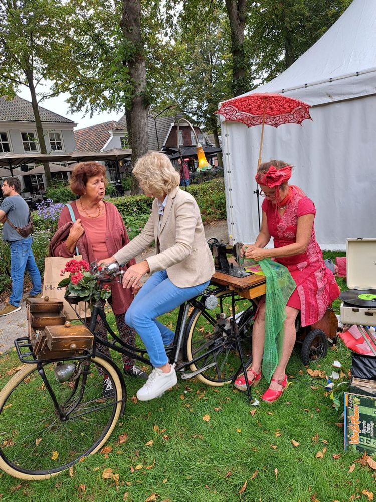 Foto van straatartiesten op het festival. Twee dames een fiets. Een van de dames fietst zodat de andere haar naaimachine kan gebruiken.