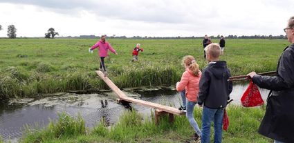 Kinderen op het Klompenpad in Benschop balanceren over een houten plankbrug over een sloot.