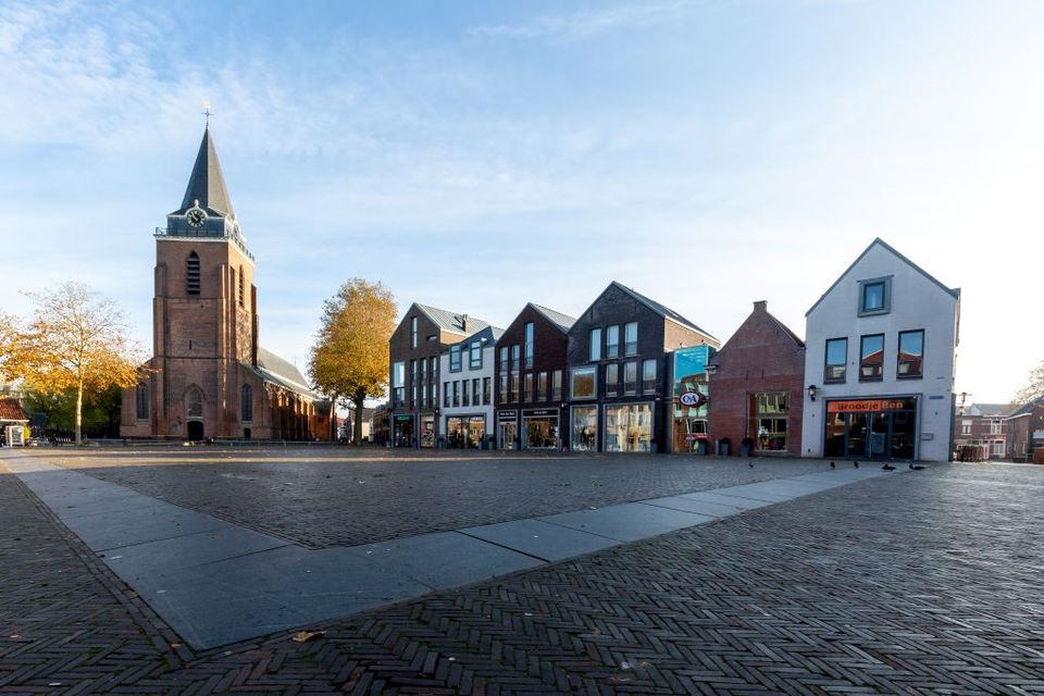Een kerk op de achtergrond, met op de voorgrond de hardstenen markering van het castellum in de bestrating. Het terrein loopt heel licht omhoog.