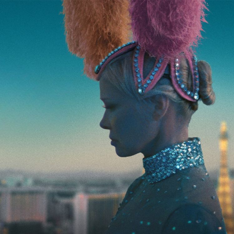 Foto van blonde vrouw in glamour en glitter top en met een hoofdtooi van roze en oranje veren.