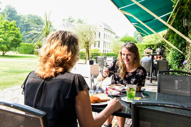 Twee vrouwen zitten op het terras van Huis Doorn een drankje te doen