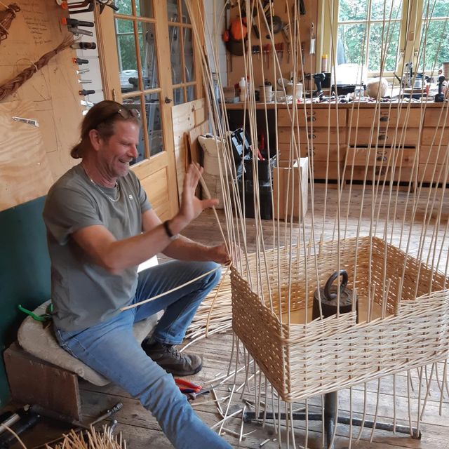 Ambachtelijke mandenmakerij De Broedkorf in Oudewater, Groene Hart. Mandenmaker vlecht met wilgentenen een handgemaakte mand in de werkplaats, omringd door traditioneel gereedschap en natuurlijke materialen.
