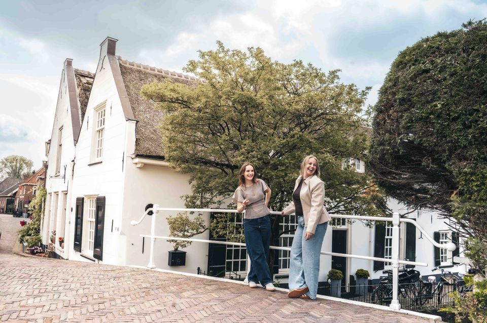 Historisch dorpsgezicht in Linschoten, gemeente Montfoort, Groene Hart, met twee wandelaars op een brug tussen monumentale witte huizen met rieten daken.