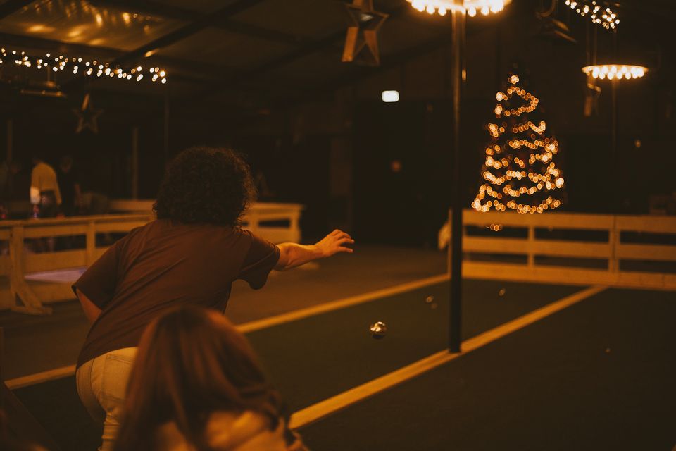 Sfeervolle indoor jeu-de-boulesbaan bij Boerderij De Boerinn, met speler die een bal werpt en warme kerstverlichting op de achtergrond – gezellige winteractiviteit in het Groene Hart.