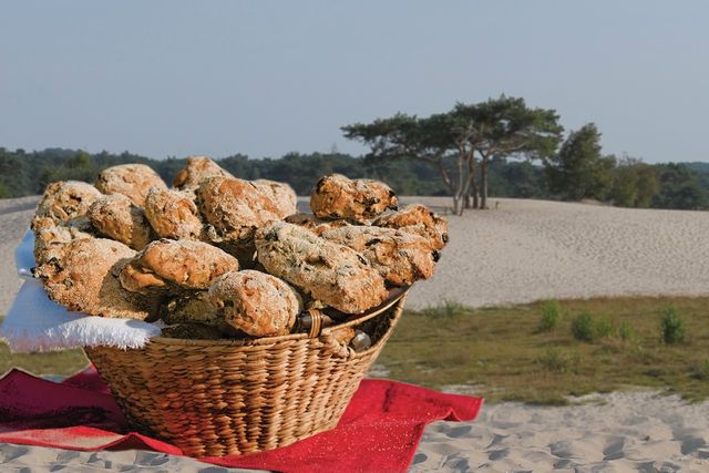 Een mand vol Soesterduintjes staat in het zand, met de Soesterduinen op de achtergrond.