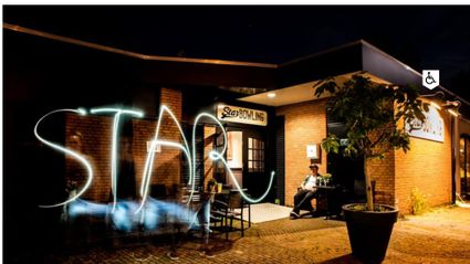 Uitgaanslocatie Star Bowling Woerden, provincie Utrecht, Groene Hart, nachtelijke sfeerfoto van het bowlingcentrum met verlichte entree, terras en lichtspoor voor de gevel.