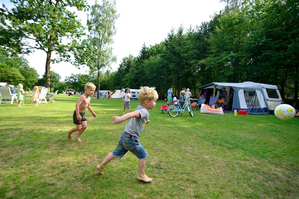Kinderen spelen voetbal op het grasveld van Allurepark De Zeven Linden in Baarn, tussen caravans en kampeerplaatsen. De foto laat de kindvriendelijke en actieve sfeer op de camping zien.