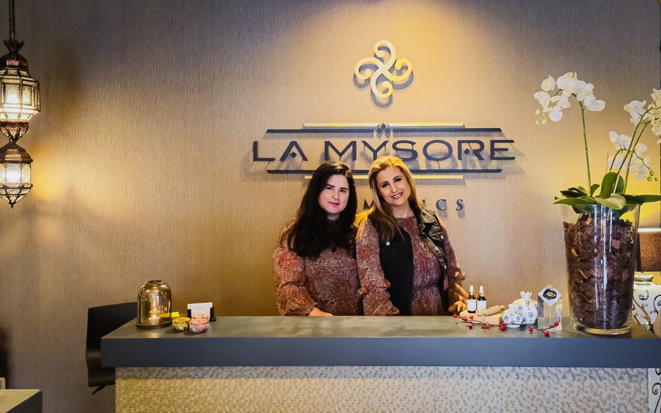 Mitra met haar dochter bij La Mysore Bussum staan samen achter de toonbank voor het logo op een koperen achtergrond