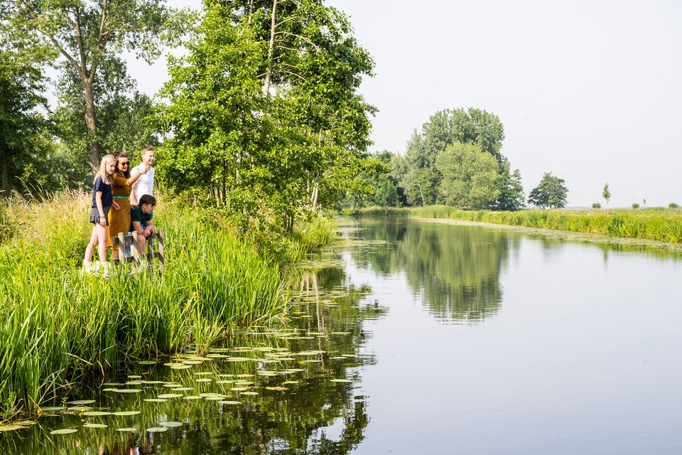 Recreatief natuurgebied Utrechtse Waarden in het Groene Hart met gezin aan de waterkant tussen riet en bomen tijdens een zomerse wandeling langs het rivierenlandschap.