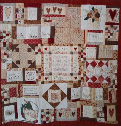 Foto van een quilt van lapjes stof in rood-wit-zand kleuren met verschillende dessins.