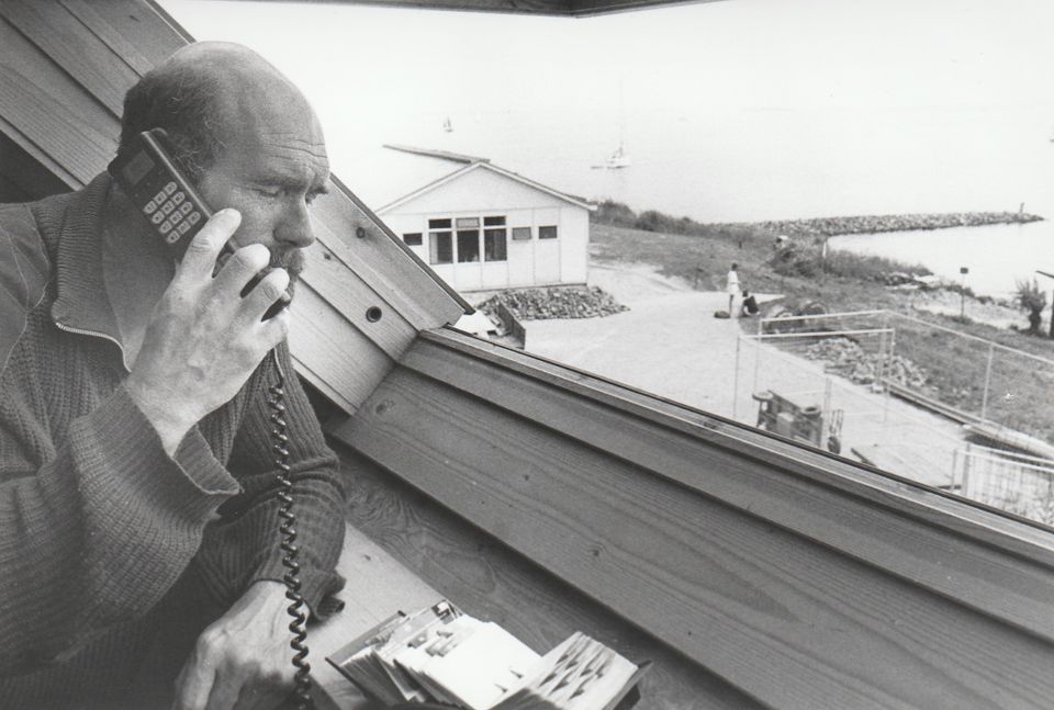 Een man telefoneert vanaf Pampus naar het vasteland. Hij staat in het dakraam van de enige woning op het eiland en kijkt uit over het water.