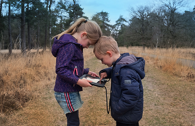 Een jongen en meisje staan met een tablet in de natuur en spelen het spel The Nature Game.
