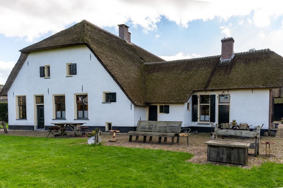 Witte, rietgedekte boerderij van Museumboerderij Het Gagelgat met bankjes en zitplaatsen op het erf.