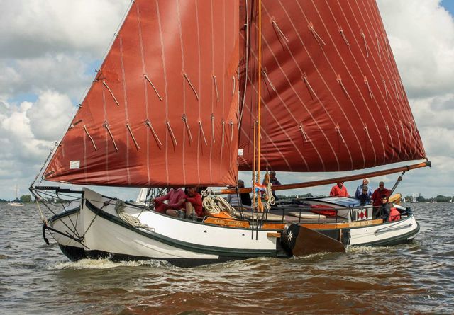 Een skûtsje in het water met bruine zeilen.
