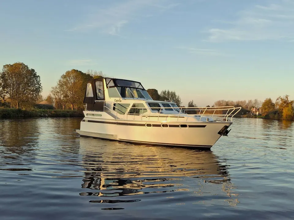 Motorjacht De Capella van REM Yachtcharter op het water met een laaghangende zon.