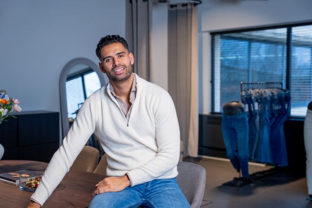 Jeanswinkel Busker Jeans in Woerden, Groene Hart, interieur met een man zittend aan tafel in de winkelruimte met op de achtergrond een presentatie van jeanskleding.