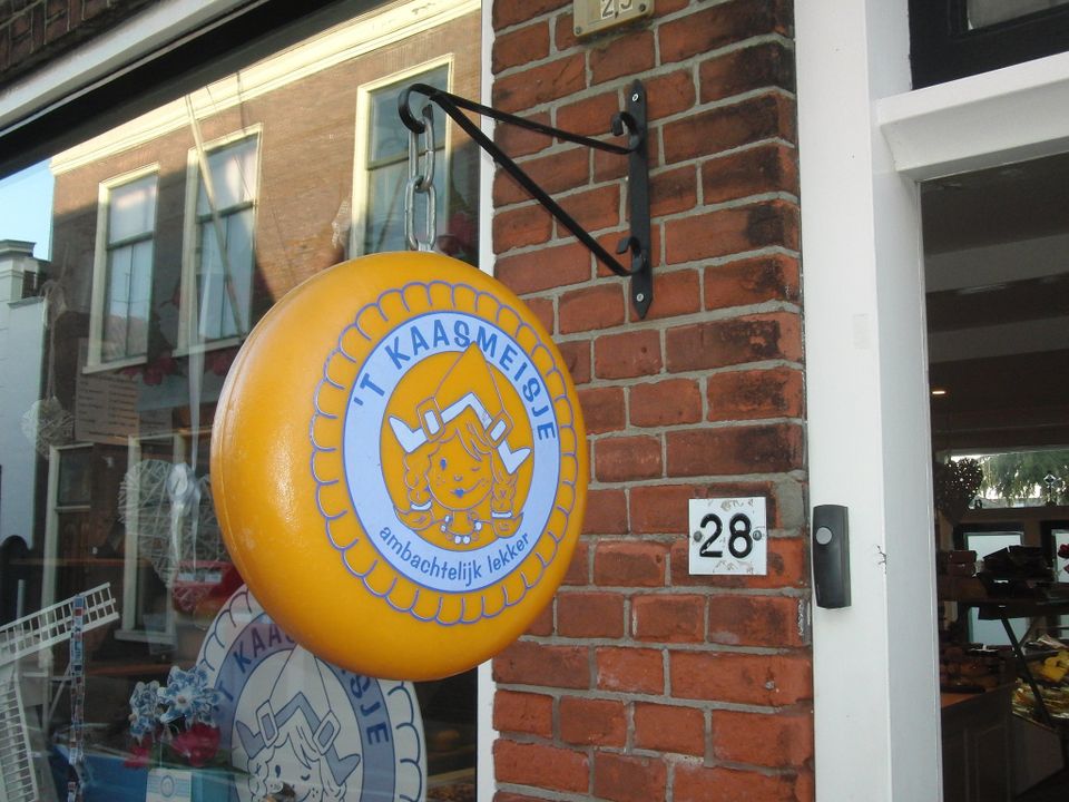 Uithangbord van delicatessenwinkel ’t Kaasmeisje in Oudewater in de vorm van een kaas met logo, bevestigd aan een bakstenen gevel.