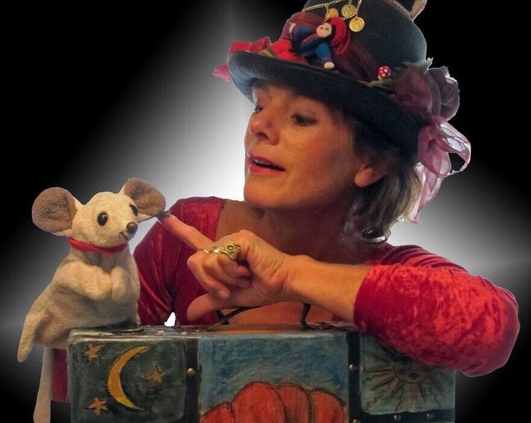 Foto van een mevrouw met een kleurrijk hoedje op en een handpop in de vorm van een muis.