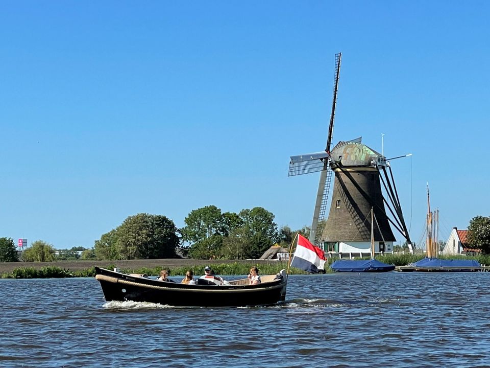 Varende sloep met een molen op de achtergrond.