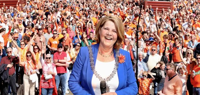 Burgemeester van Bijsterveld op een podium op de Markt met mensen zwaaiend achter haar