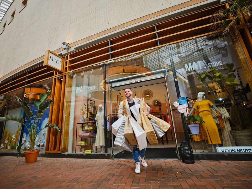 Een man staat voor een winkel in Hilversum met zijn handen vol tassen.
