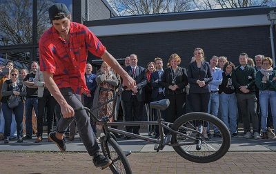 Een jongen doet een truc op een BMX terwijl achter hem allemaal mensen naar je kijken.