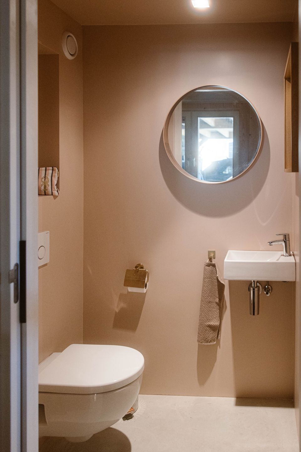 Moderne toiletruimte van Aliedas Annex bij Esti Yoga in Lopik, Groene Hart, met wandtoilet, witte wastafel, ronde spiegel en beige muren.