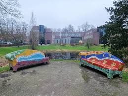 Foto van kleurrijke mozaïekbankjes in ronde vorm met op de achtergrond de achterkant van het gemeentehuis in Oisterwijk.