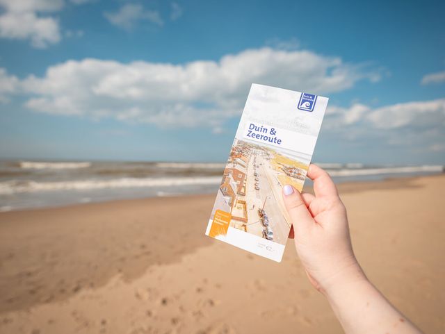 Afbeelding van de Duin & Zeeroute folder op het strand.