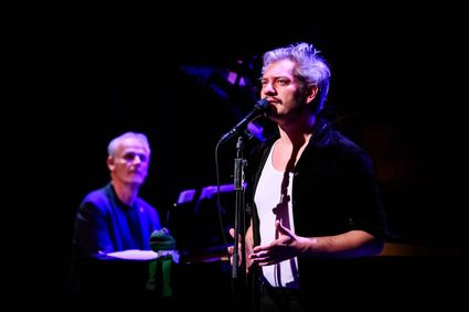 Theatervoorstelling Ramses enzo, Maarten Heijmans en Cor Bakker, theaterzaal, Groene Hart, zanger staat in spotlicht aan microfoon terwijl pianist op de achtergrond begeleidt tijdens een muzikale hommage aan Ramses Shaffy.