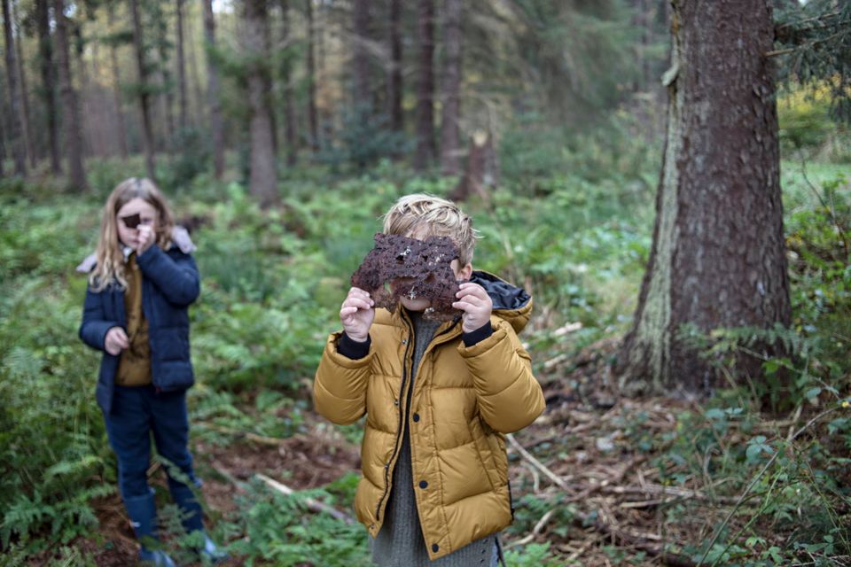 Kinderen spelen in het bos met bladeren en houden deze voor hun gezicht.