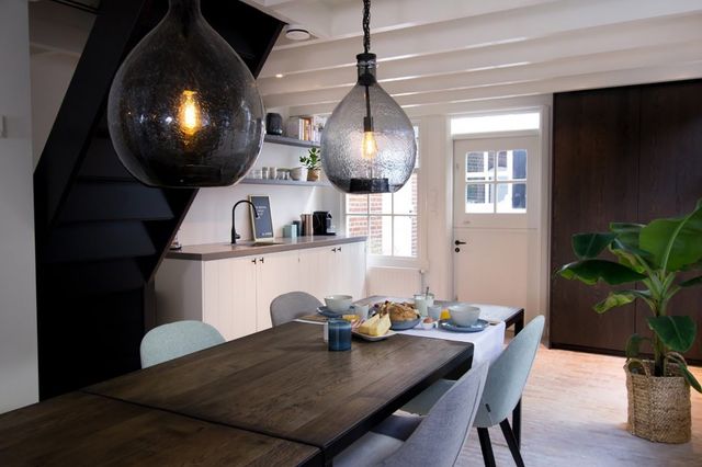 Eetkamer met ingedekte lange donker houten tafel met stoelen en een licht keukenblok.