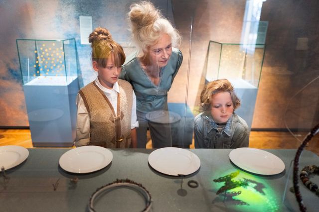 Eine Frau schaut sich mit ihren zwei Enkelkindern Exponate im Museum an.