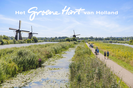 UNESCO Werelderfgoed Kinderdijk in Molenlanden, Zuid-Holland, met historische windmolens, wandelpad langs het water, rietkragen en recreanten op een zonnige dag in het Groene Hart van Holland.